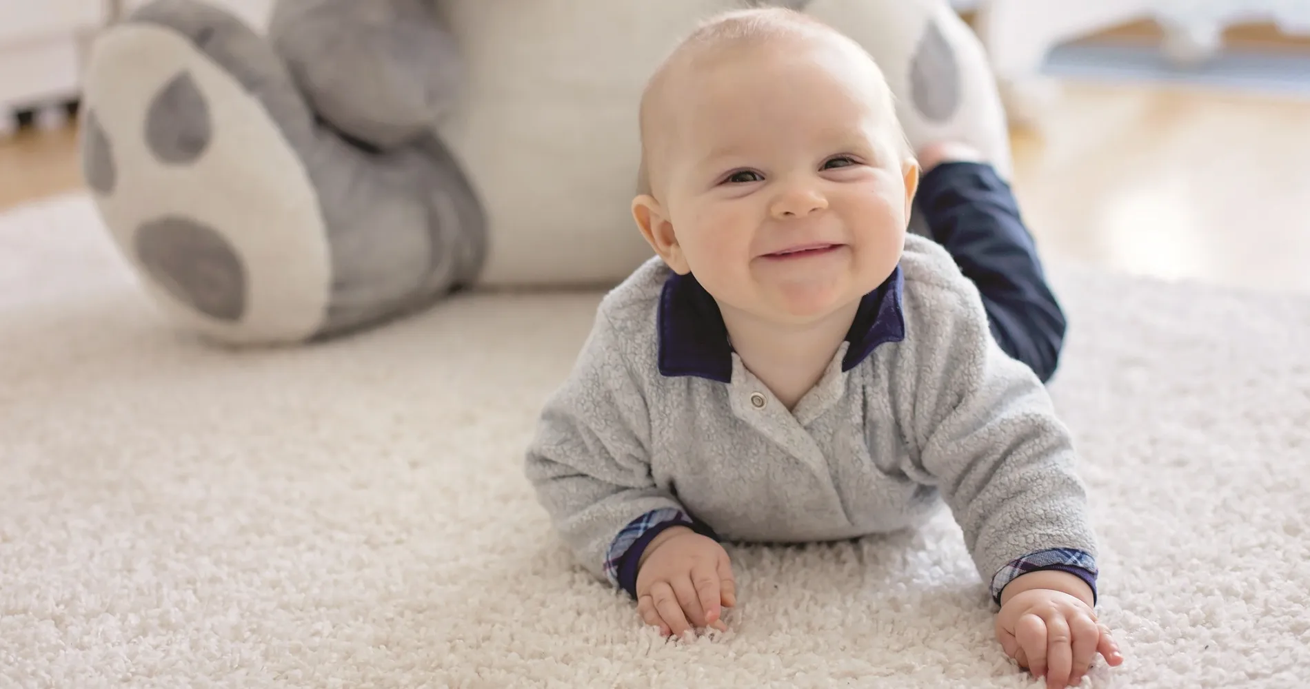 Baby smiling while laying on the white fluffy carpeted floor
